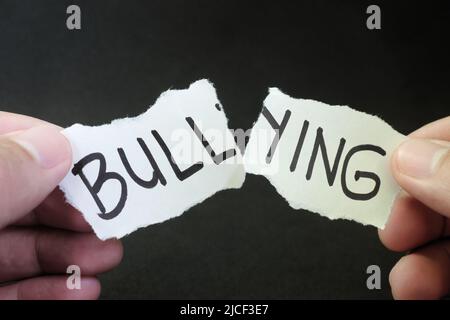 Fight and stop bullying concept. Hand tearing paper with word bullying in dark black background. Stock Photo