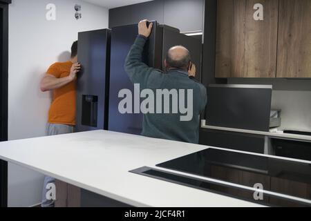 Two technicians installing an american fridge in a new modern kitchen. Stock Photo