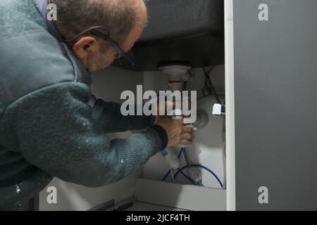 Mature plumber installing sink siphon in domestic kitchen. Stock Photo