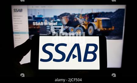 Person holding smartphone with logo of Swedish steel company SSAB AB on screen in front of website. Focus on phone display. Stock Photo