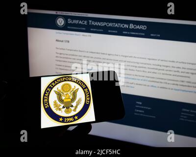Person holding cellphone with seal of American Surface Transportation Board (STB) on screen in front of webpage. Focus on phone display. Stock Photo