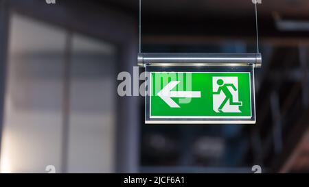 Essen, Germany - Mar 26, 2022: Illuminated emergency exit sign. Arrow pointing to the left. Stock Photo