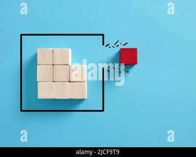 Concept of overcoming barriers, individuality and independence in business. Red wooden cube breaking through the obstacle. Stock Photo