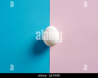 One white egg on pink and blue duotone background. Stock Photo