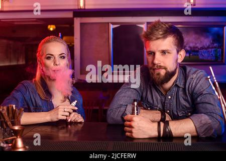 A man and woman smoking electronic cigarette in a vape bar. Stock Photo