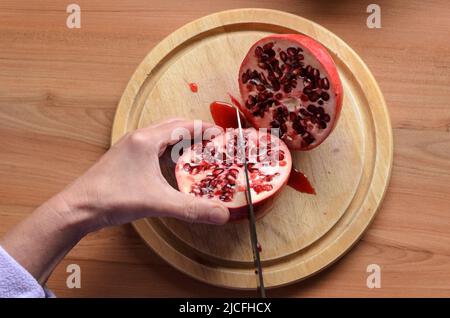 Cutting and opening a red Pomegranate fruit (Punica granatum) with a knife on a wooden board Stock Photo