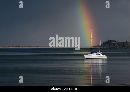 A boat appears to be the pot of gold at the end of a beautiful rainbow on a stormy day. Stock Photo