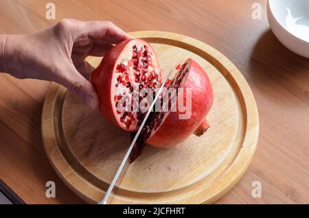 Cutting and opening a red Pomegranate fruit (Punica granatum) with a knife on a wooden board Stock Photo