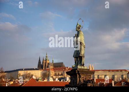 St. John of Nepomuk with halo, bronze statue on Charles Bridge, Prague Castle behind, Hradcany, Prague, Czech Republic Stock Photo