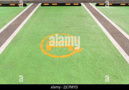 Yellow electric car symbol on green asphalt. Electric vehicle charging parking Stock Photo