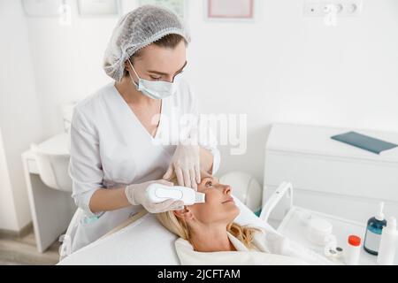 Female cosmetologist performing female face skin massage procedure in ...