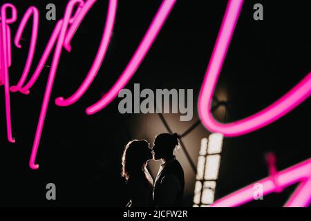 Young couple in love in darkness under pink neon sign Stock Photo