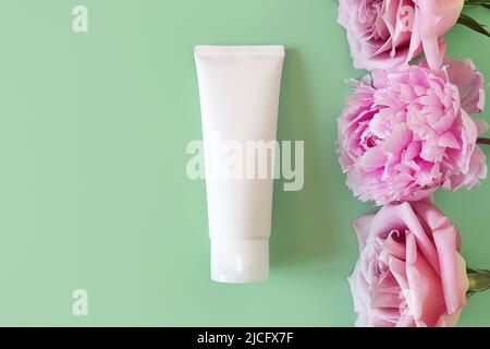 Cosmetic bottle container tube, pink roses and peony on green background. Mockup of white squeeze bottle plastic for branding of medicine or cosmetics Stock Photo