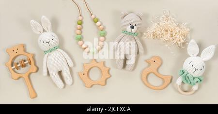 Baby toys banner. Crocheted handmade bunny and teddy bear, teether beads and rattles in eco style on a brown background with raffia clouds. Infant bab Stock Photo