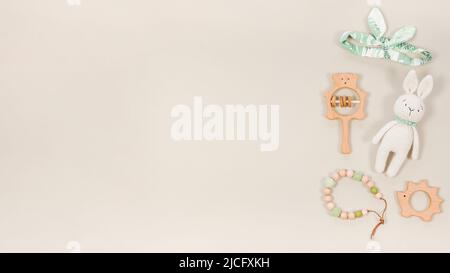 Baby toys and accessories background with copy space. Cute wooden teethers, handmade knitted bunny, baby beads and a headband on a pastel brown banner Stock Photo