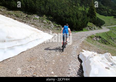 e-bike rider young man, shortly after the Karwendelhaus, in the direction of kleiner Ahornboden, on the side there is still the snow of the previous winter Stock Photo