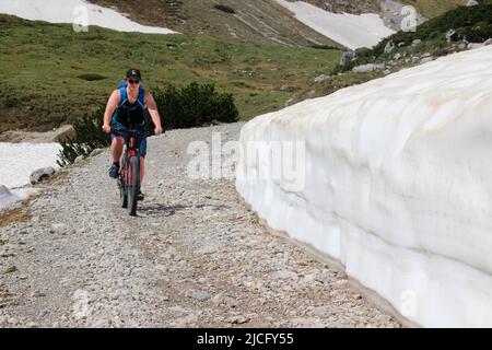 e-bike rider young man, shortly after the Karwendelhaus, in the direction of kleiner Ahornboden, on the side there is still the snow of the previous winter Stock Photo