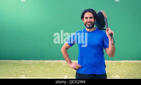 Monitor of padel holding black racket with copy space. Class to student on outdoor tennis court. Man paddel player playing a match in the open. Racque Stock Photo