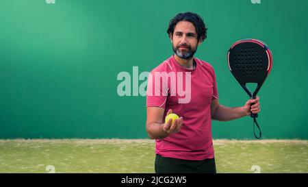 Monitor of padel holding black racket with yellow tennis ball in the hand. Class to student on outdoor tennis court. Man paddel player playing a match Stock Photo