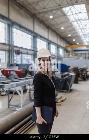 Portrait of female chief engineer in modern industrial factory holding tablet. Stock Photo