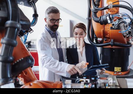 Robotics engineers with tablet dicussing and desinging modern robotic arm in factory. Stock Photo