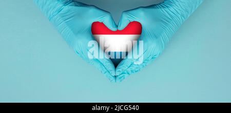 Doctors hands wearing blue surgical gloves making hear shape symbol with luxembourg flag Stock Photo