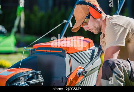 Male Caucasian Gardener focused on Inspecting His Equipment Before Starting Mowing the Lawn on His Client’s Backyard. Closeup of a Professional Garden Stock Photo