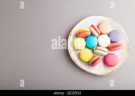 Multicolored macaroons on ceramic plate on gray pastel background. top view, copy space, still life, flat lay. Breakfast, morning, concept. Stock Photo