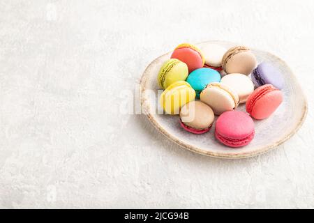 Multicolored macaroons on ceramic plate on gray concrete background. side view, close up, still life, copy space. Breakfast, morning, concept. Stock Photo