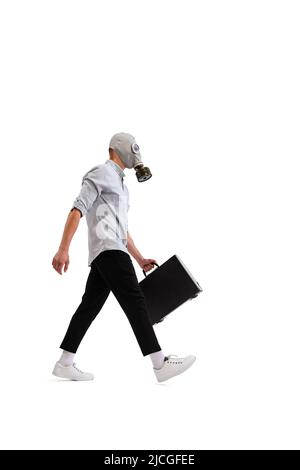 Portrait of young employee, office worker wearing gas mask, carrying suitcase with imporatant business paper isolated over white background. Stock Photo