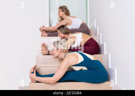three young women practicing yoga poses stretching in studio Stock Photo