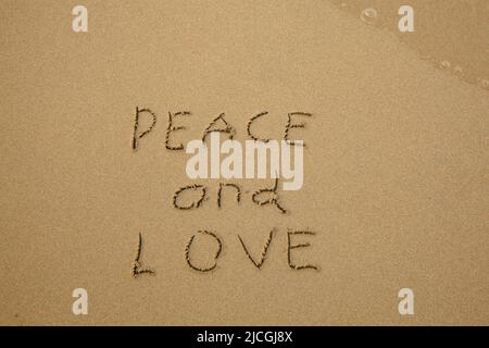 Peace and Love - handwritten on the soft beach sand. Stock Photo