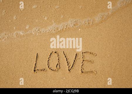 LOVE - handwritten on the soft beach sand. Stock Photo