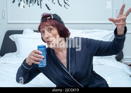 An elderly woman in a stylish Mercedes baseball cap drinks Pepsi and shows the symbol of victory with her fingers. Turkey, Istanbul, May 29, 2022. Stock Photo