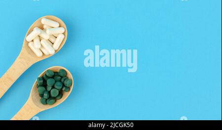 White and green pills in wooden spoons on a blue background Stock Photo