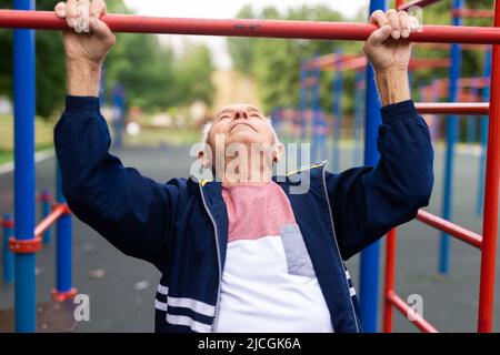 Sportive old man doing pull-ups outdoors Stock Photo