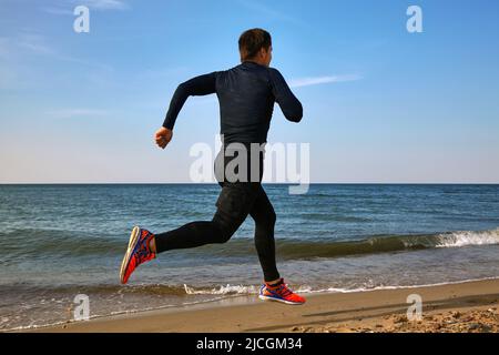 Man runner on the seashore in sports outfit. Cardio jogging Stock Photo