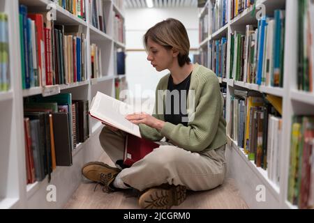 Focused woman teacher in casual clothes sits with textbook, prepares study for students at lesson. Stock Photo