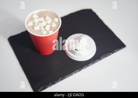 Red paper cup of coffee with marshmallows on a black tray. Stock Photo