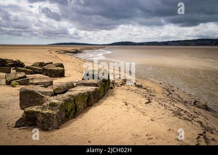 Limestone rock and sand along the Kent channel flowing into Morecombe Bay at low-tide with Grange-over-Sands in the background, Lancashire, England Stock Photo