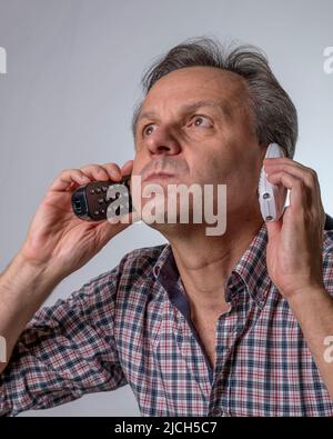 A man with two phones is fed up with being harassed over the phone with unwanted business proposals Stock Photo