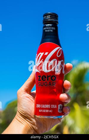 Barcelona, Spain - June 1, 2022: Aluminum Coca-Cola bottle in hand against blue sky and palm trees. Coke brand Stock Photo