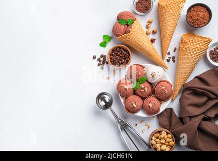 Balls of chocolate and cream ice cream, waffle cups, chocolate, coffee and nuts on a gray background. Stock Photo