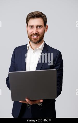 Cheerful man in suit holding laptop over grey background Stock Photo