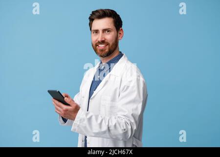 Cheerful man doctor holding mobile phone over blue studio background Stock Photo