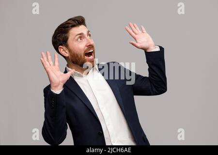 Handsome man wearing suit with a beard puts his hands to the side of his mouth and screams Stock Photo