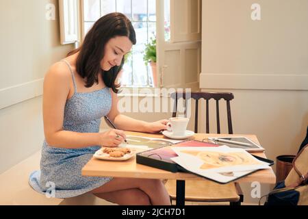 Woman draws while she is drinking coffee in a coffee shop Stock Photo