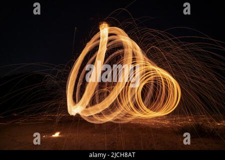 Spinning and burning Steel wool sparkle fire in the circle shape with long speed shutter shoot glowing light line to the ground. Stock Photo