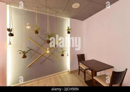 Corner of a restaurant dining room with pale pink walls decorated in jungle motifs with reeds, bamboo, hanging plants and lamps Stock Photo