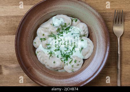 Appetizing dumplings stuffed with potatoes and mushrooms with sour cream and green dill on a ceramic plate, close up, top view. Homemade Ukrainian cui Stock Photo
